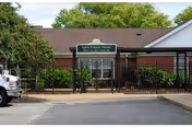 Front exterior of St. Francis Home — a single-story brick building with a green entrance sign, black metal fence, and surrounding greenery.