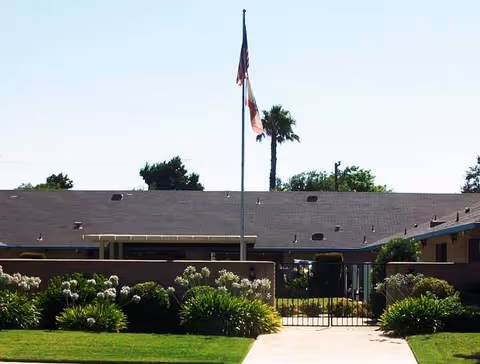 Front view of a low one-story building with a central flagpole, gated entrance and landscaped lawn.