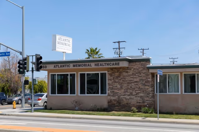 Exterior view of Atlantic Memorial Healthcare Center building at a street corner with traffic lights, cars, and a clear blue sky.