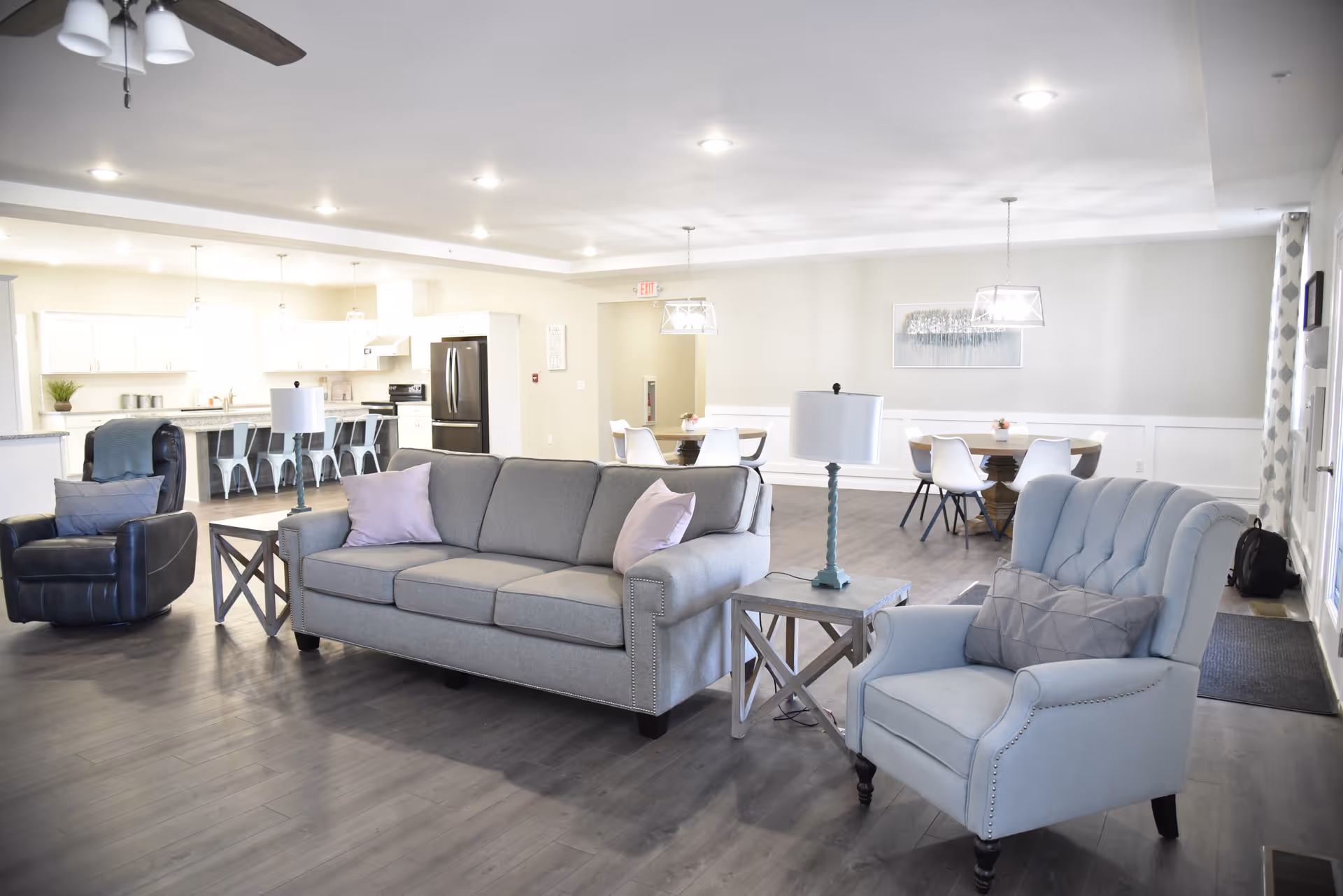 Open communal living area with sofas, chairs, dining tables, and a bright kitchen in the background.