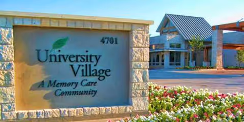 Stone sign reading University Village Memory Care Community with building entrance and flower landscaping.