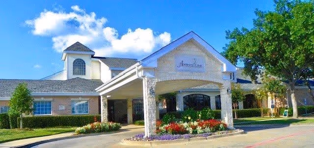 Front exterior view of Appletree Court facility with a covered entrance, landscaped flower beds, and a clear blue sky with some clouds.