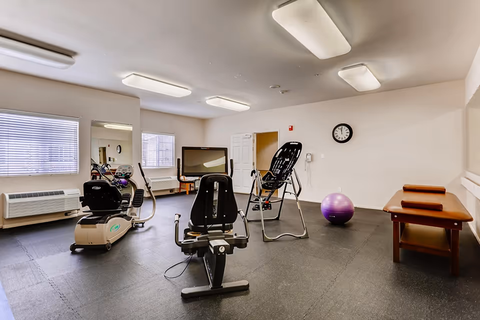 An exercise/therapy room with recumbent bikes, an inversion table, a purple stability ball, and a treatment bench.
