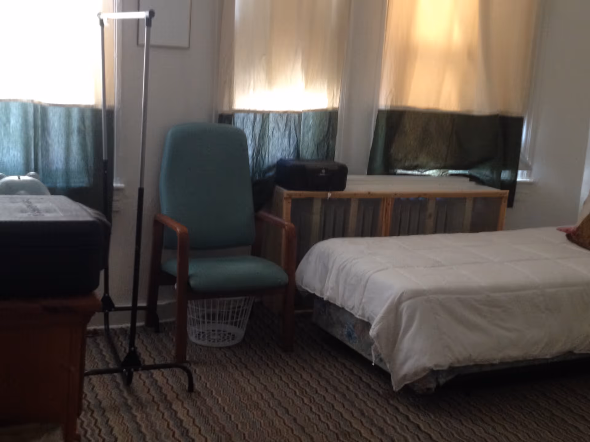 Small bedroom with a single bed, a green armchair, and windows with curtains.