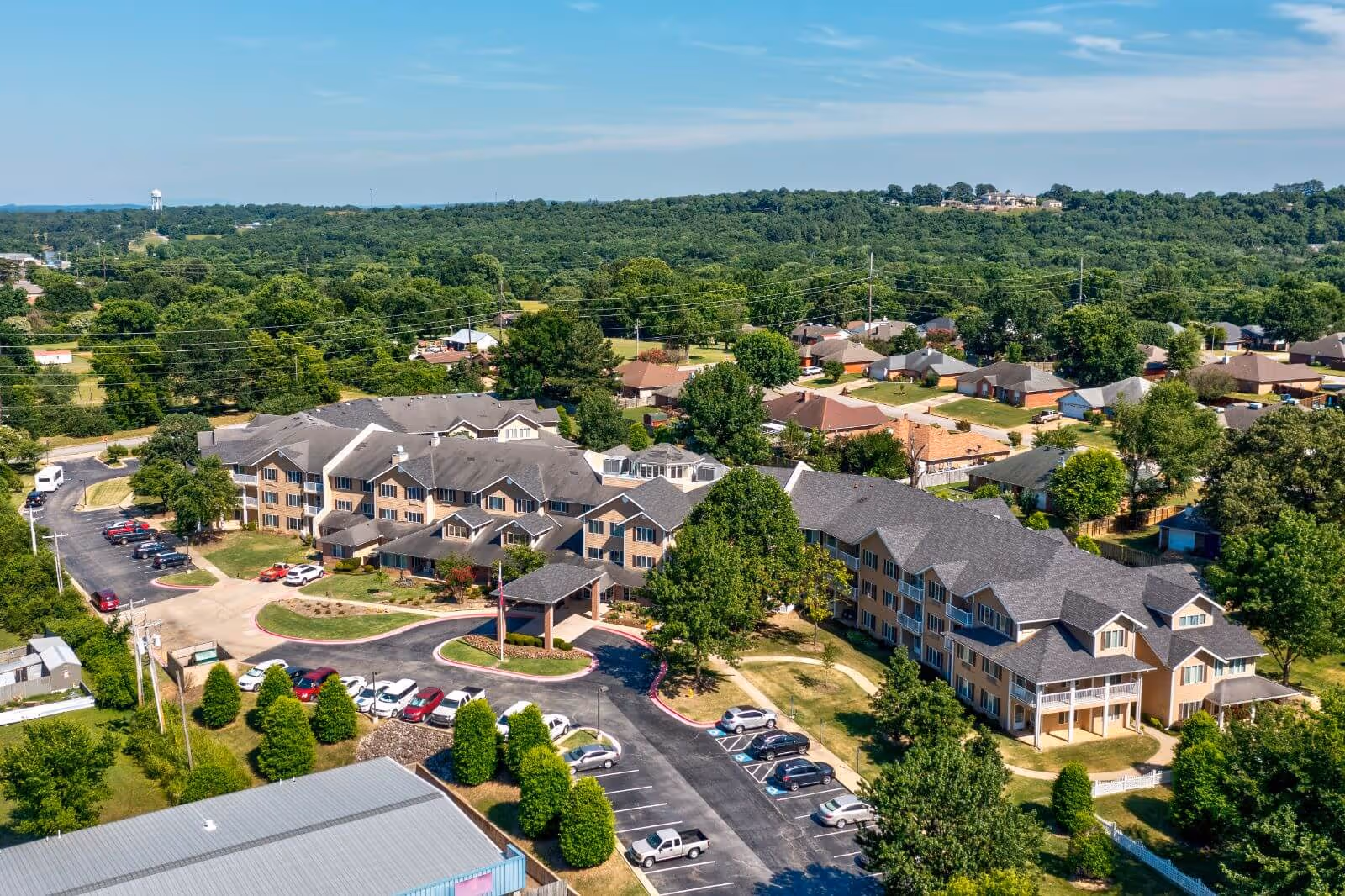 Aerial view of a multi-building, three-story senior living complex with an entrance canopy, parking lots, landscaped grounds, and surrounding neighborhood.
