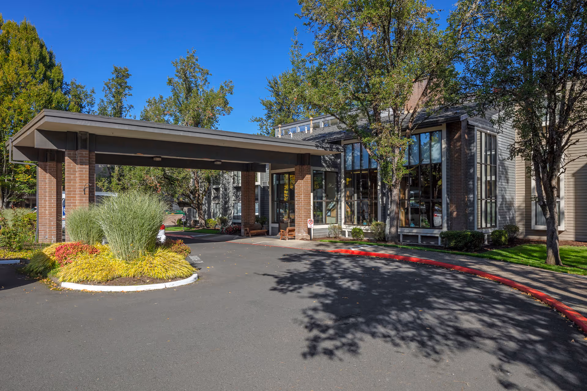 Covered porte-cochere entrance of a retirement residence with landscaped islands and large glass windows.