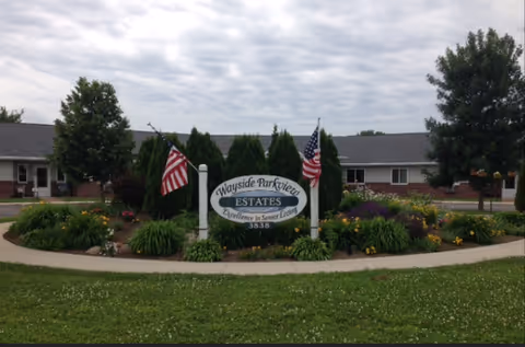 Front exterior of Wayside Parkview Estates with landscaped entrance sign and American flags.