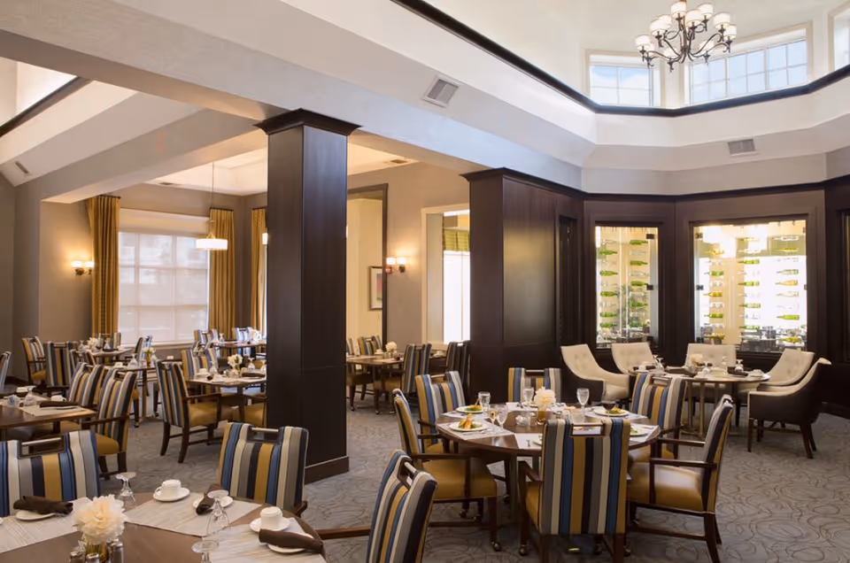 Spacious, well-appointed dining room with multiple set tables, striped upholstered chairs, a chandelier, and a wine display cabinet.