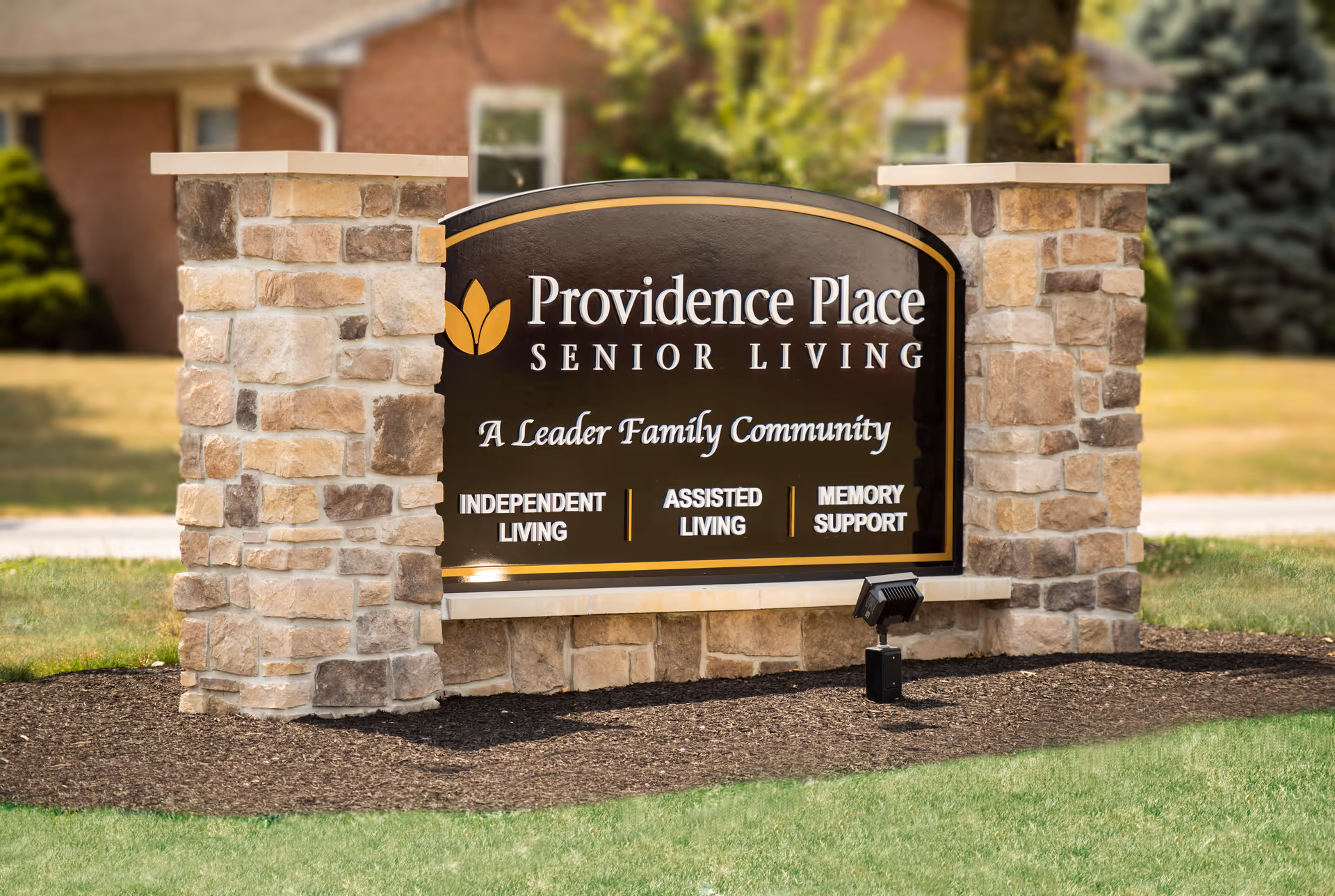 Stone monument sign on a lawn reading "Providence Place Senior Living" with services listed below.