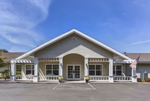 Single-story senior living facility front entrance with porch, columns, and an American flag.