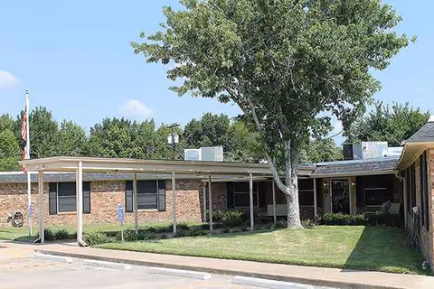 Exterior view of a single-story brick senior facility with a covered entrance and lawn.