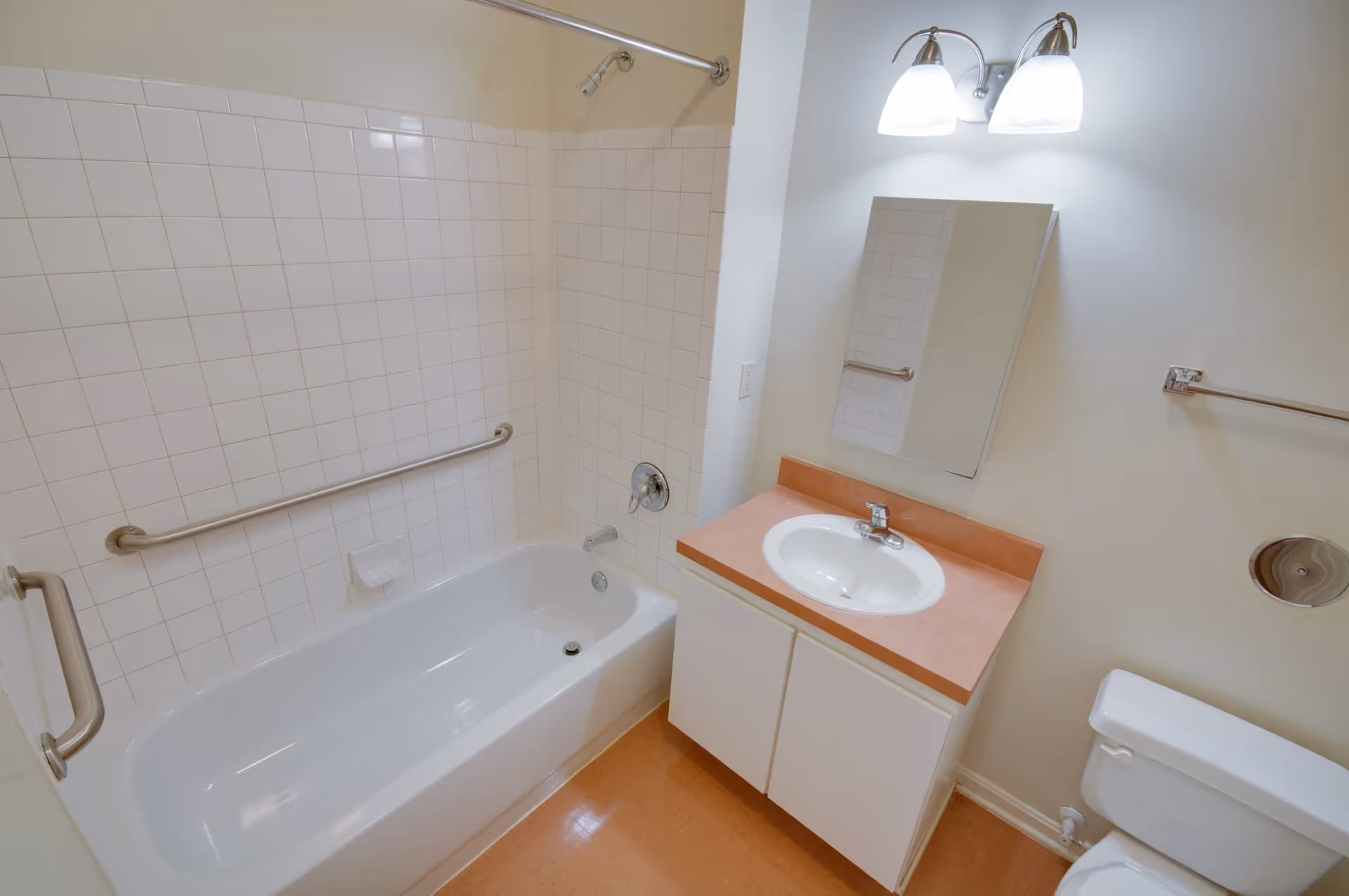 Clean bathroom with a bathtub and tiled shower, grab bars, sink vanity with mirror and a toilet.