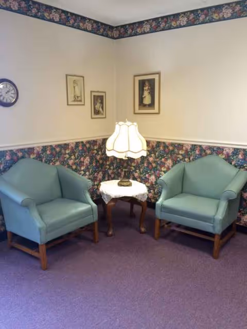 Two light teal armchairs flank a small table with a lamp in a cozy lounge.