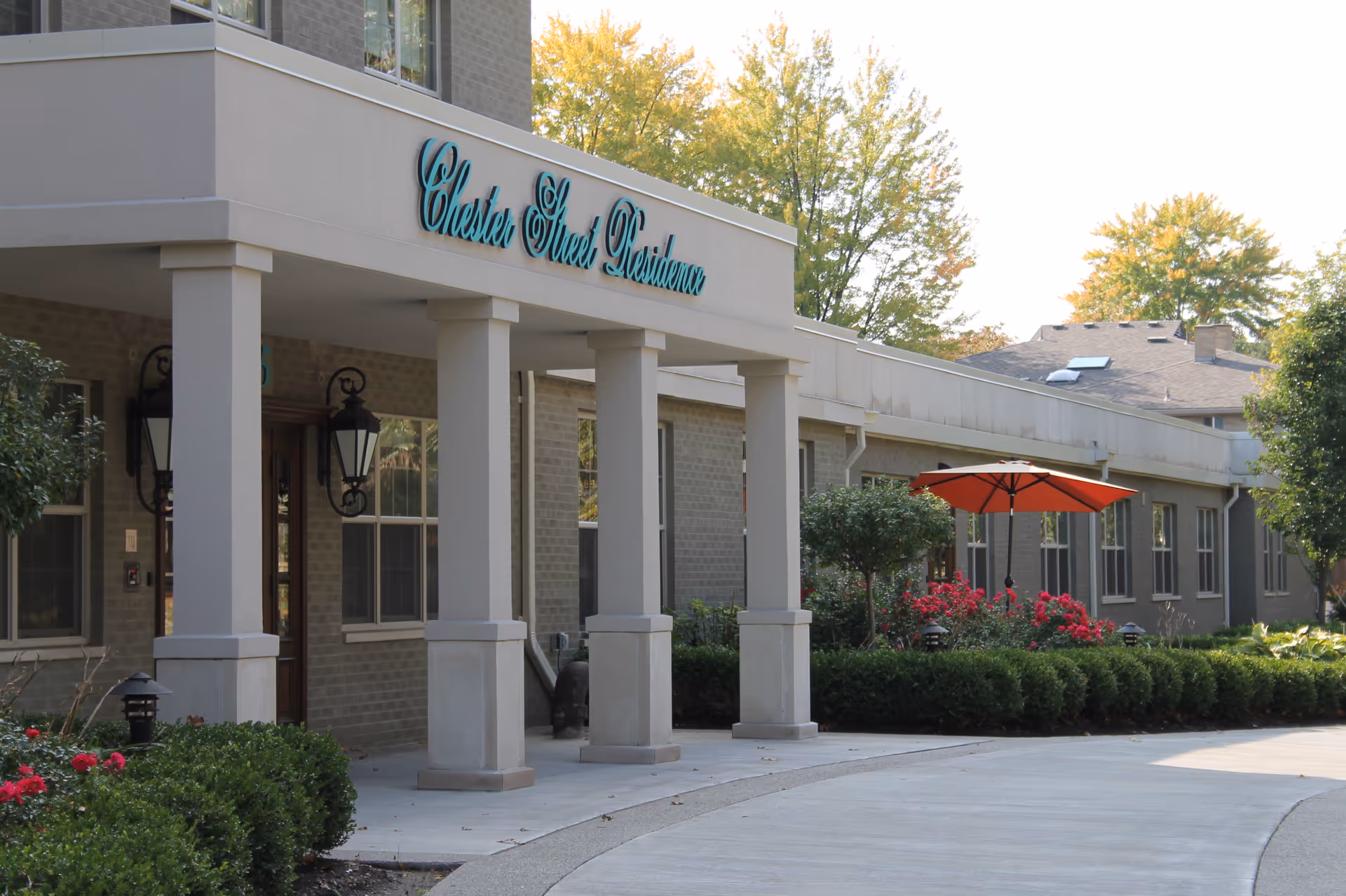 Exterior view of Chester Street Residence with a covered entrance, columns, and a red umbrella seating area.