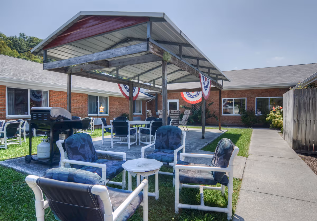 Outdoor covered patio courtyard with seating, tables, a grill, and patriotic bunting in front of a brick senior living building.