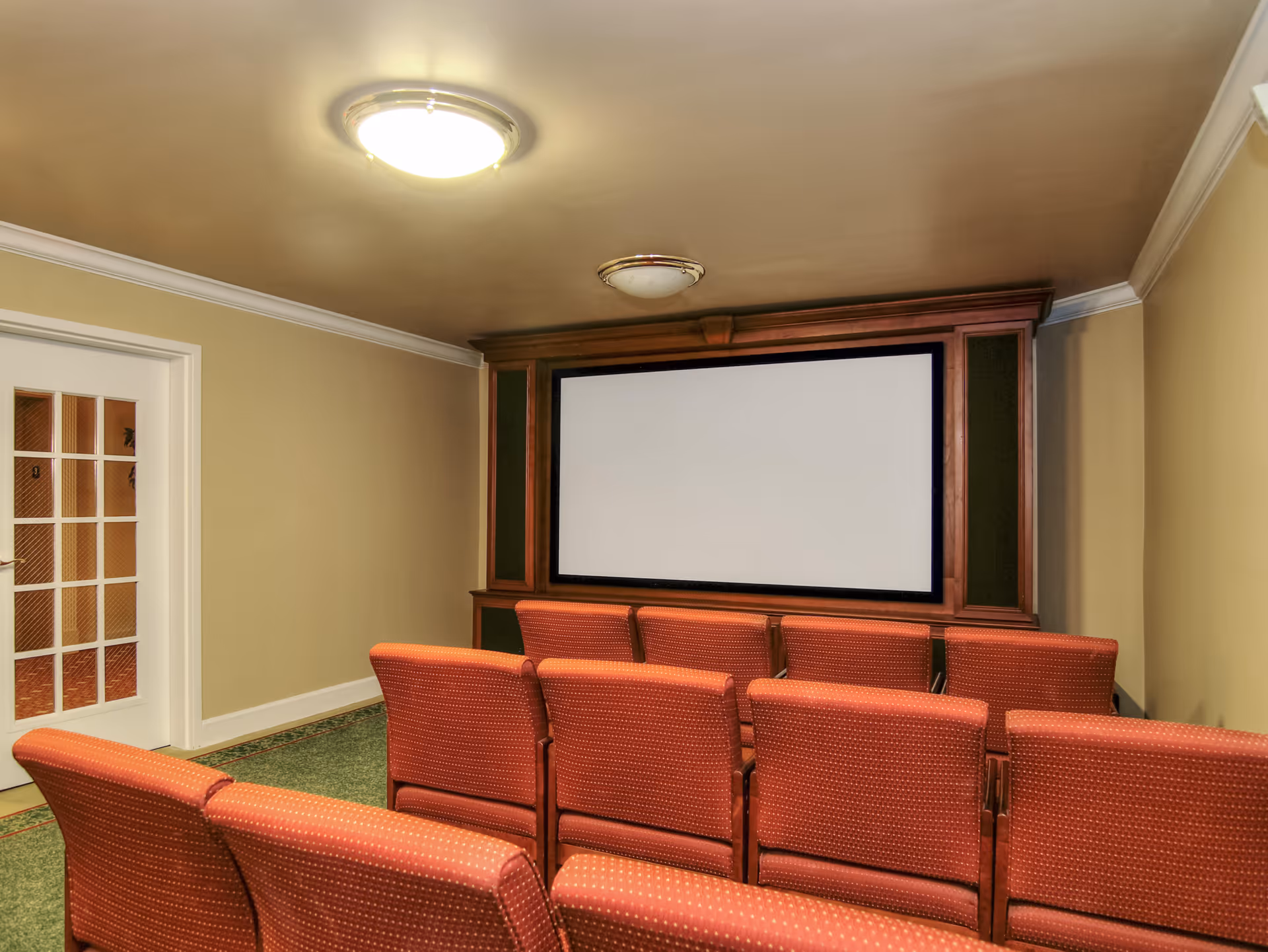 Small screening room with rows of red upholstered chairs facing a large blank projection screen.