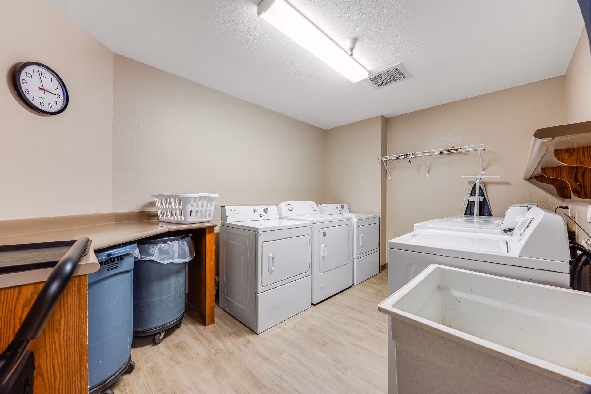 A communal laundry room with multiple washers and dryers, a folding counter, laundry baskets and a utility sink.