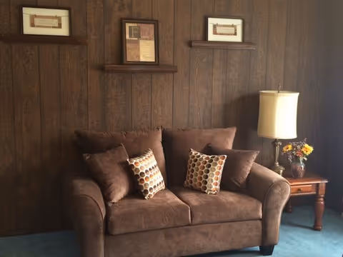 Brown sofa with patterned pillows sits against dark wood-paneled wall in living area.