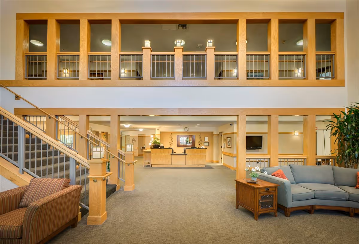 A spacious lobby area featuring a staircase, comfortable seating, and a reception desk. The design includes wooden accents and large windows, creating a welcoming atmosphere.