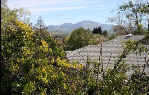 Rooftop and shrubbery overlook with distant mountains under a clear sky.