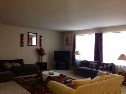 Marigold Home living room with beige couches, coffee table, TV, and large windows.