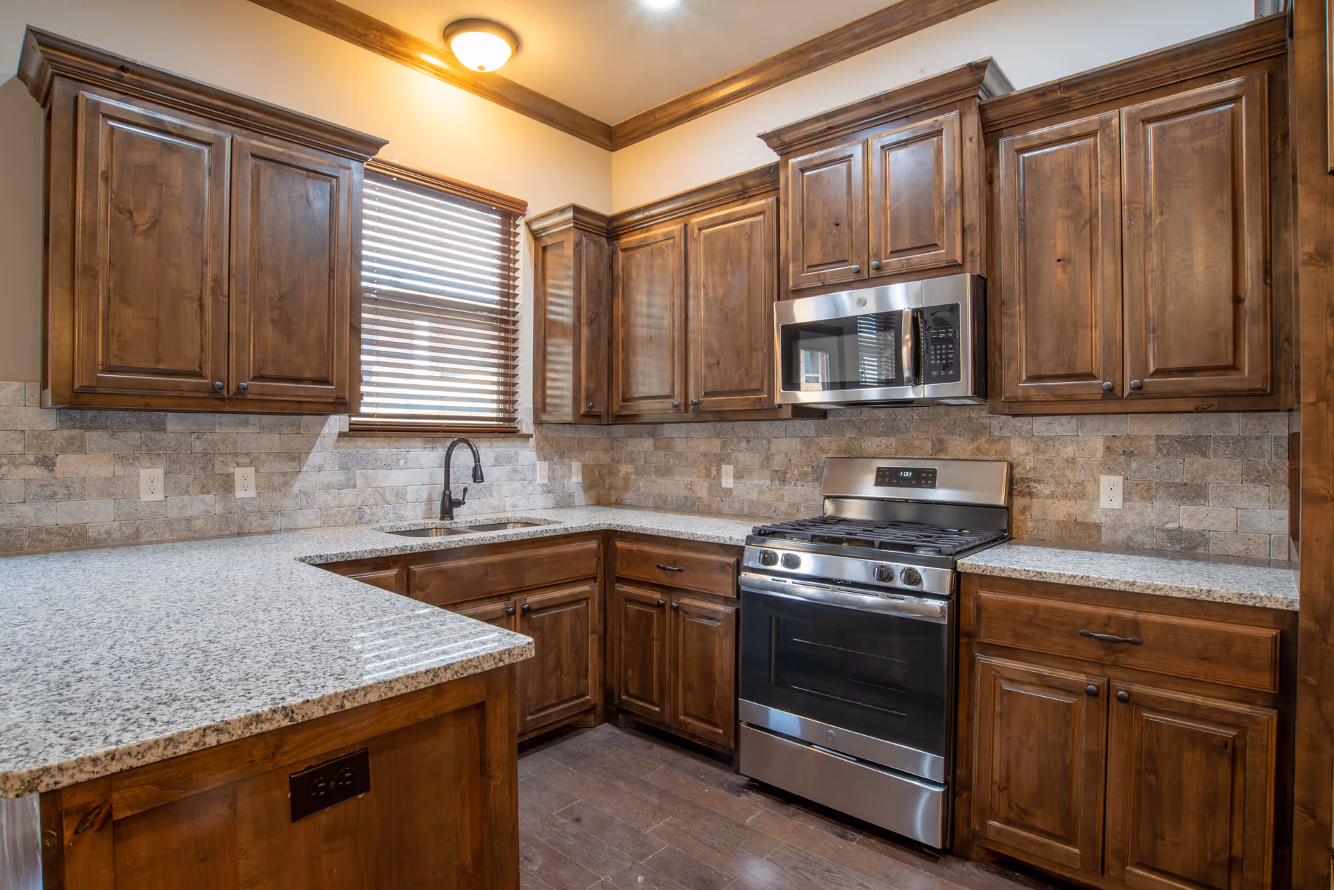 Modern kitchen with wooden cabinets, granite countertops, a stainless steel stove and microwave, and a window above the sink.