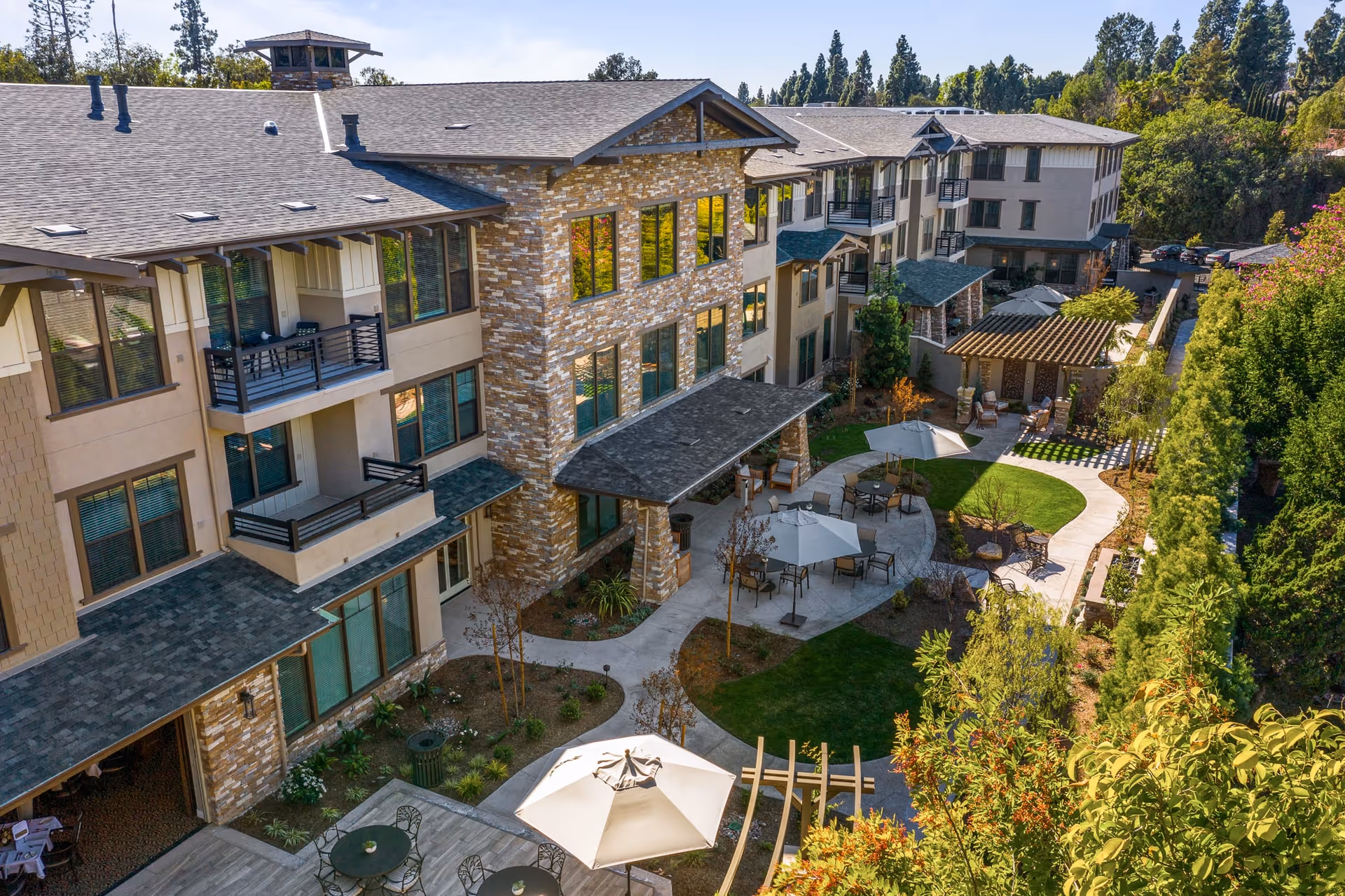 Aerial view of a multi-story senior living building surrounding a landscaped courtyard with patios, umbrellas, walkways, and seating.