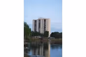 Tall apartment building across a lake with trees and blue sky.