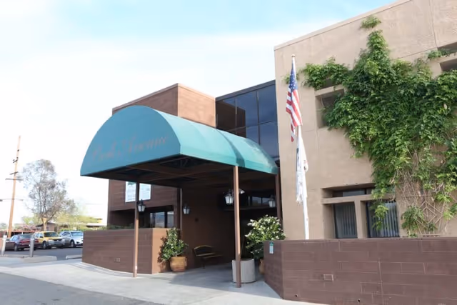 Front entrance of Park Avenue Health and Rehabilitation showing a green awning over the doorway, an American flag, and ivy on the building.
