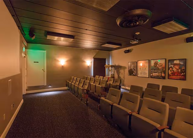 Small private theater room with rows of upholstered seats, movie posters on the wall, and a projection screen.