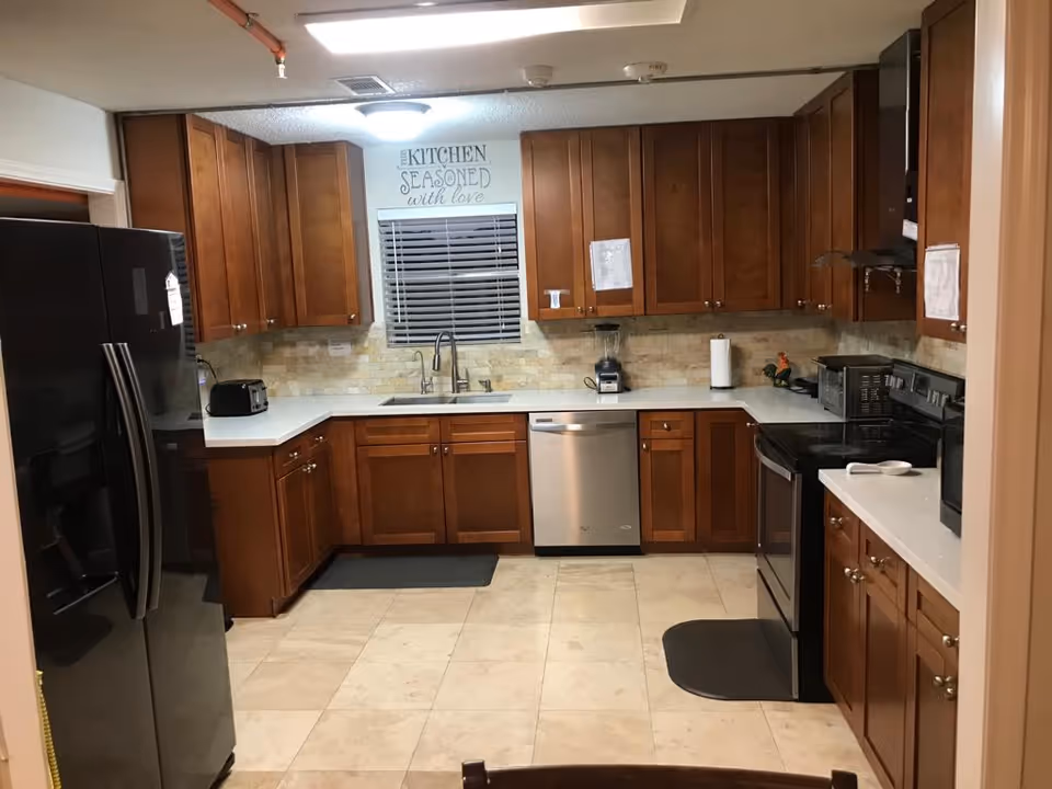 Well-lit kitchen with wooden cabinets, a window over a sink, stainless steel appliances and light tiled floor.