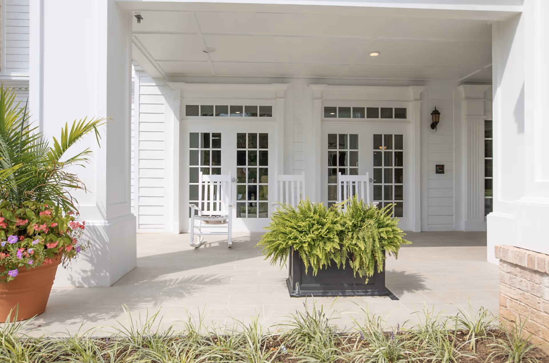 Covered entrance porch with white French doors, two white rocking chairs, and potted greenery.