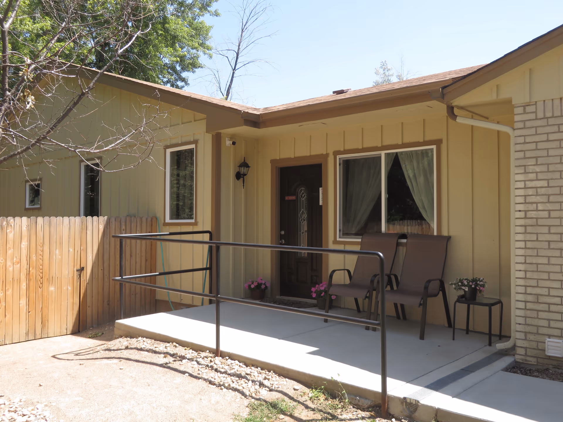 Exterior view of ThriveCare Assisted Living front porch with two chairs and potted plants.