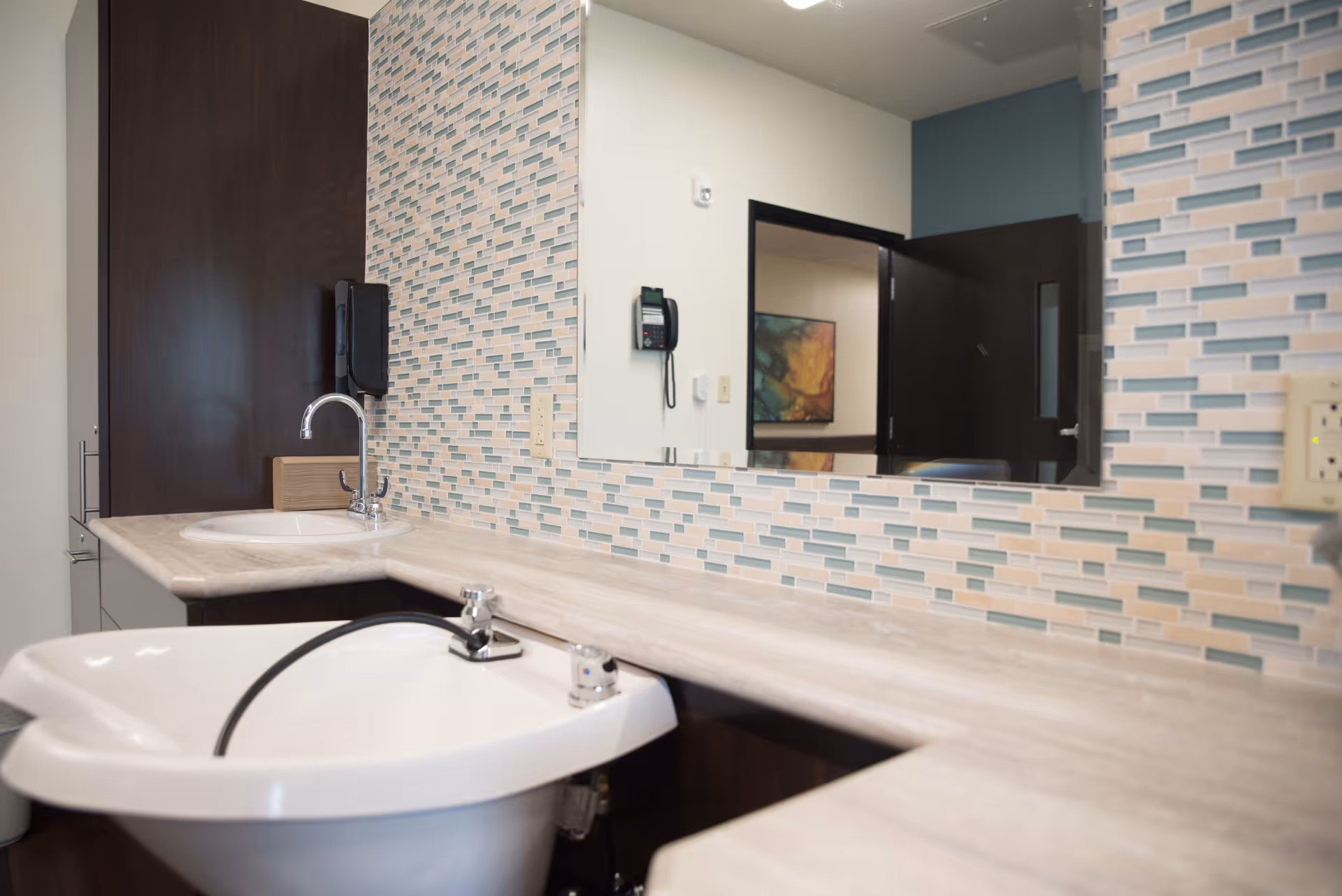 A tiled vanity area with two sinks, a large mirror, and a phone on the wall in a facility bathroom/grooming space.