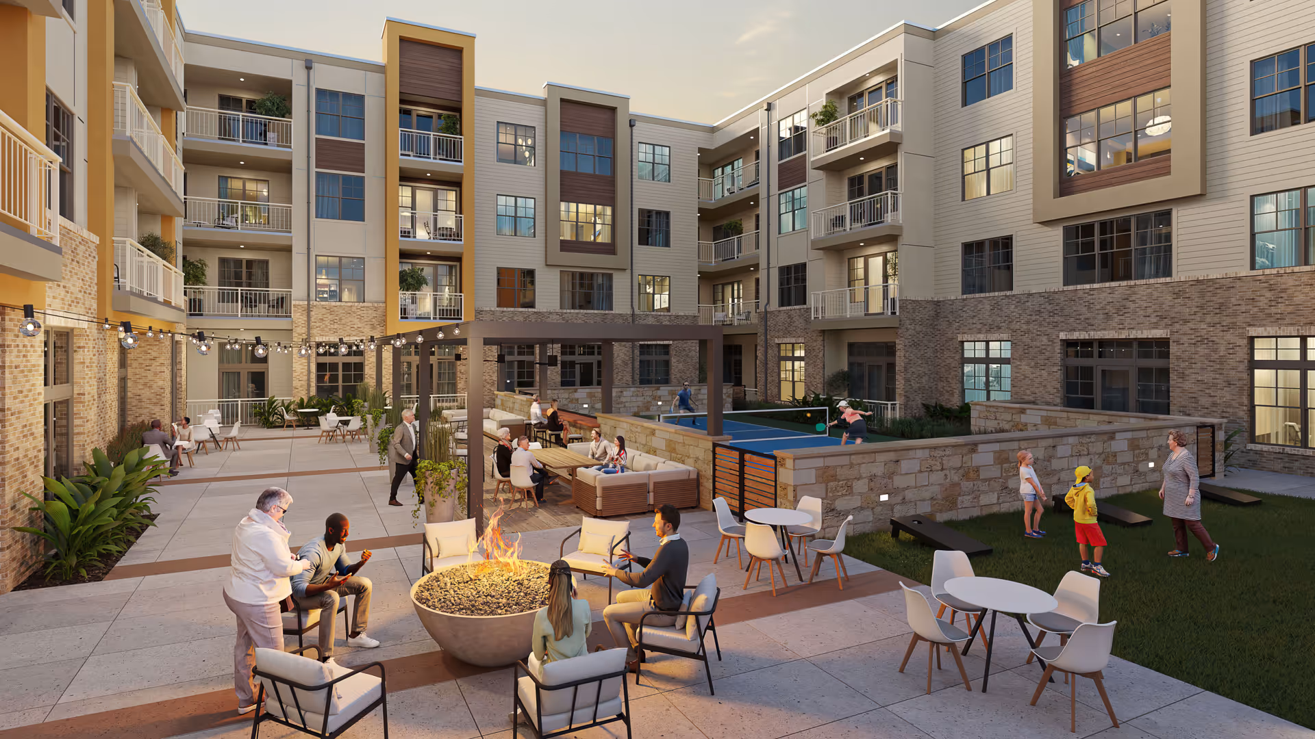 Outdoor courtyard area of The Jovie at Pflugerville senior living facility with people sitting around a fire pit, others playing table tennis, and children playing on the grass. The courtyard is surrounded by a multi-story building with balconies and large windows, decorated with string lights and outdoor seating.