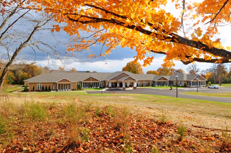 Front exterior of the Webb House Retirement Center building framed by orange autumn leaves in the foreground.