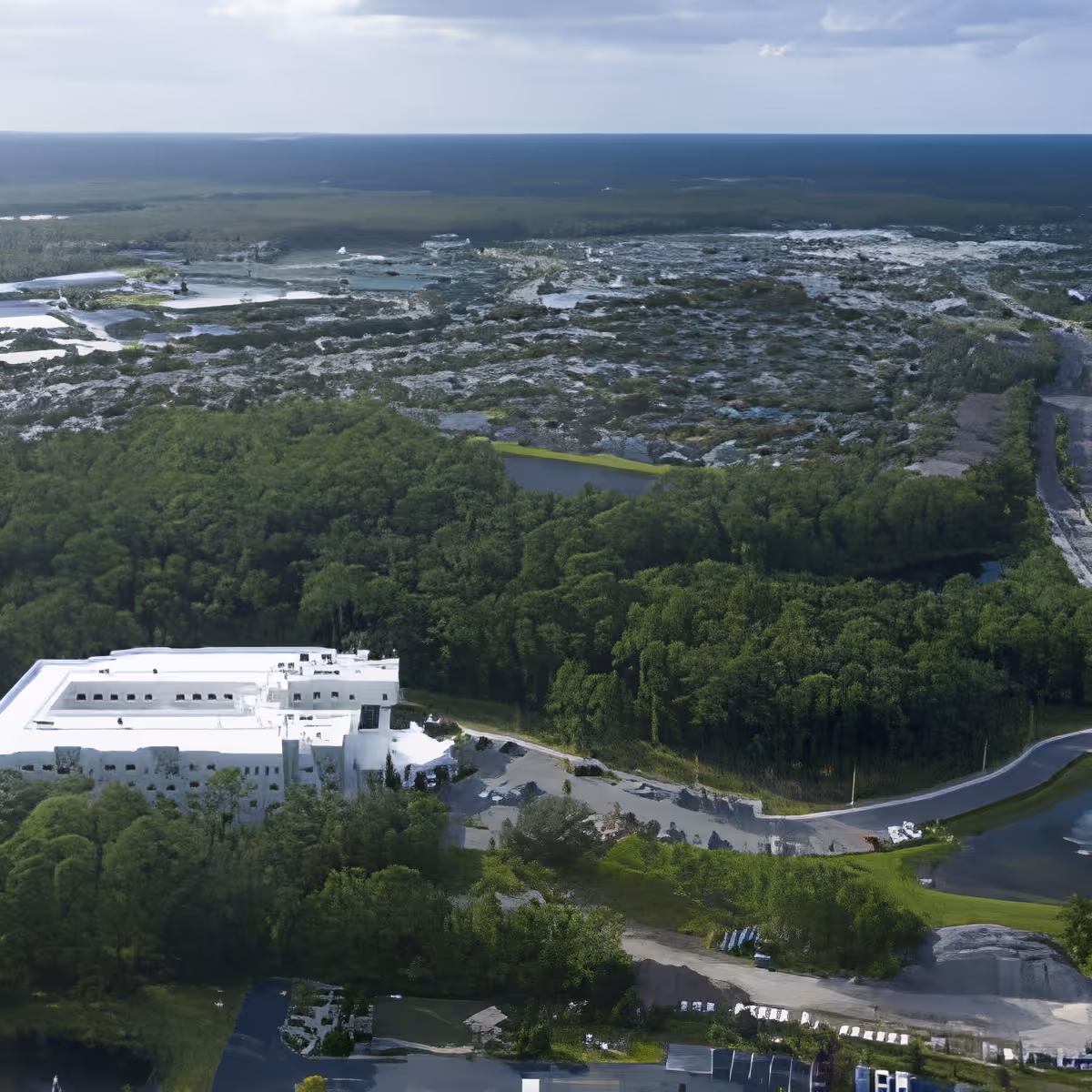 Aerial view of a white senior living facility building surrounded by dense trees, roads, and wetlands.