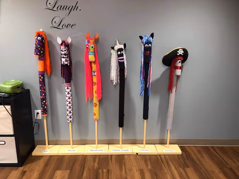 Colorful sock puppets on wooden stands line a wall with Laugh, Love in a senior facility.