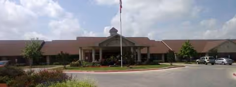 Front exterior view of a single-story senior care facility with flagpole and parking.