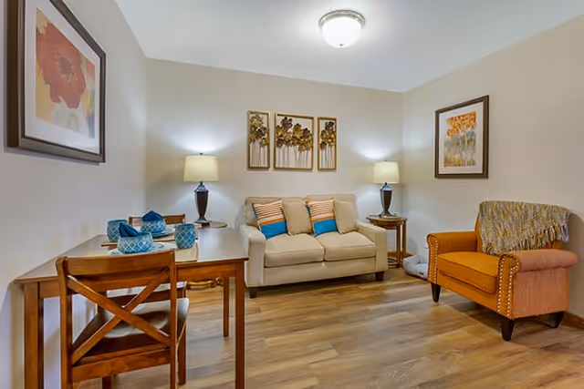 Cozy living room with a loveseat, armchair, small dining table, lamps, and wall art.