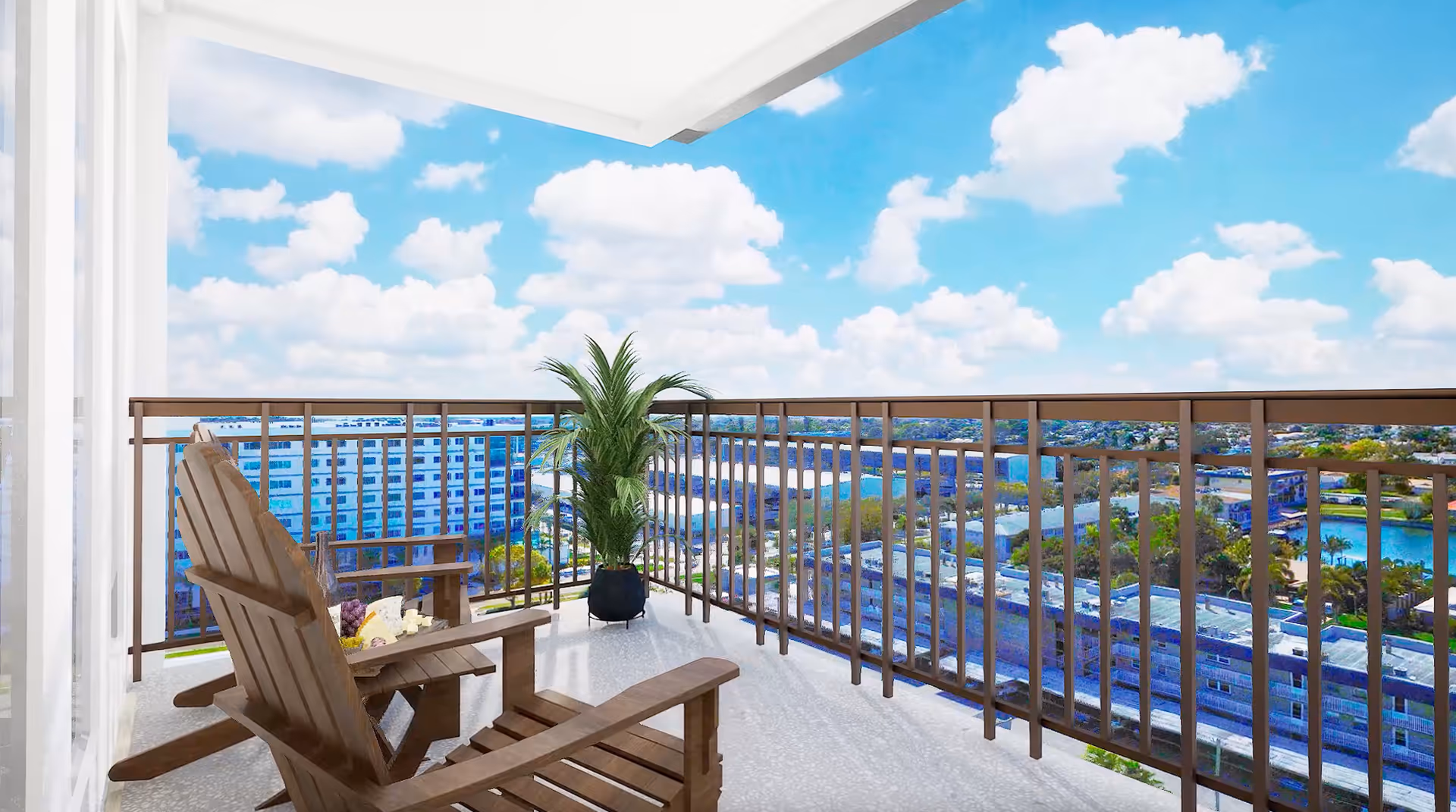 A balcony with two wooden chairs and a small table holding a bottle and some snacks. There is a potted plant in the corner and a view of buildings, water, and a partly cloudy blue sky in the background.