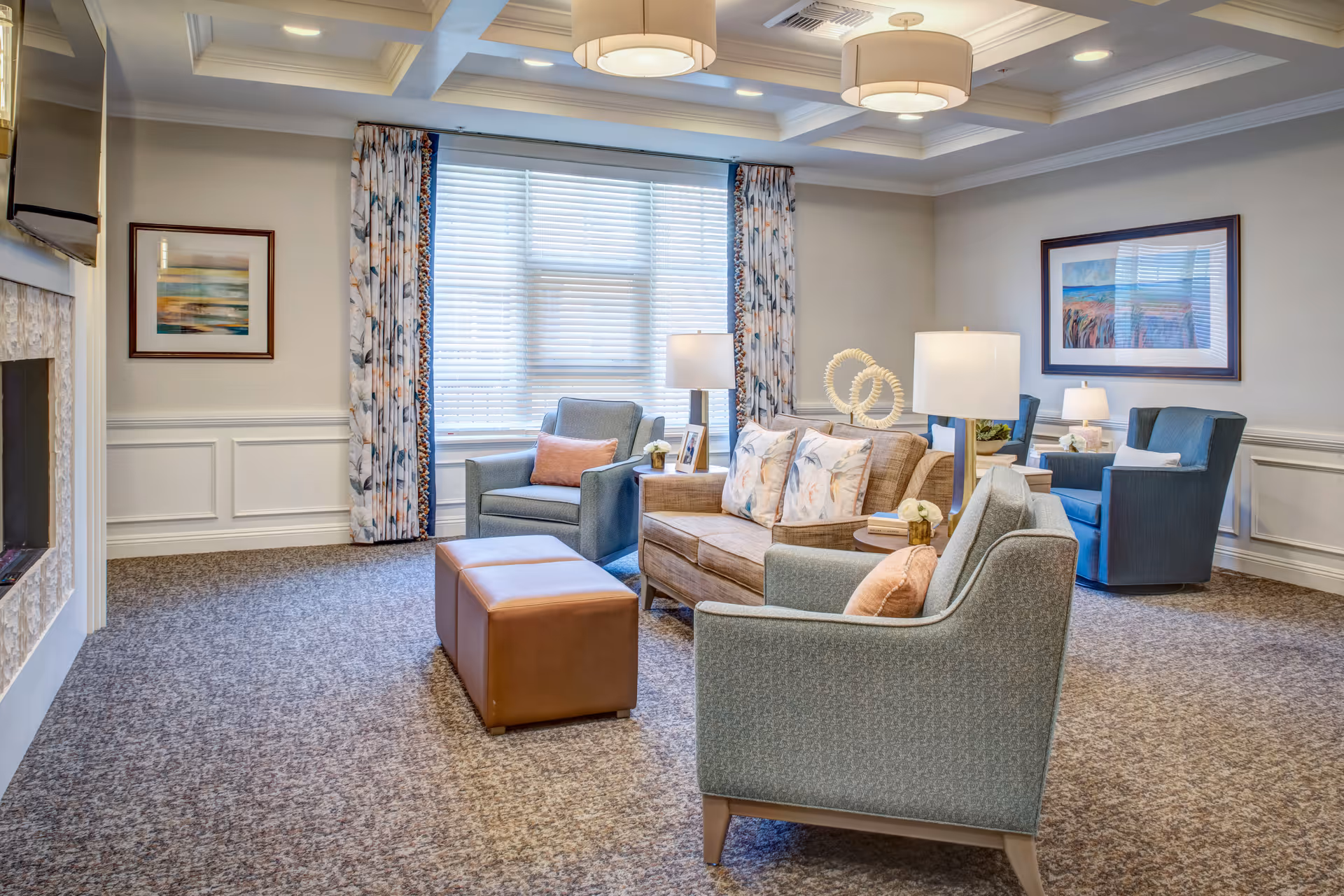 Bright, well-furnished lounge with sofas, armchairs, lamps, an ottoman, and framed wall art.