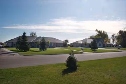A single-story senior living facility exterior with green lawns and trees along a street.