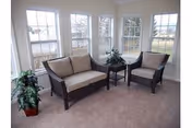 Bright sunroom with a loveseat and armchair around a small side table with plants in front of multiple windows.