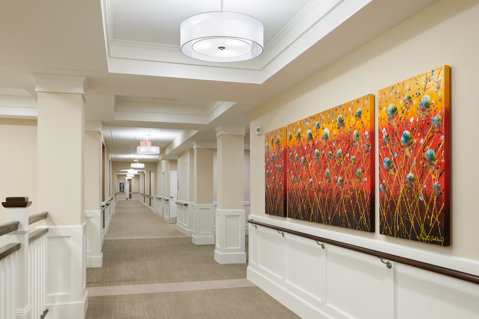 Well-lit interior hallway with handrails and a colorful three-panel painting on the right wall.