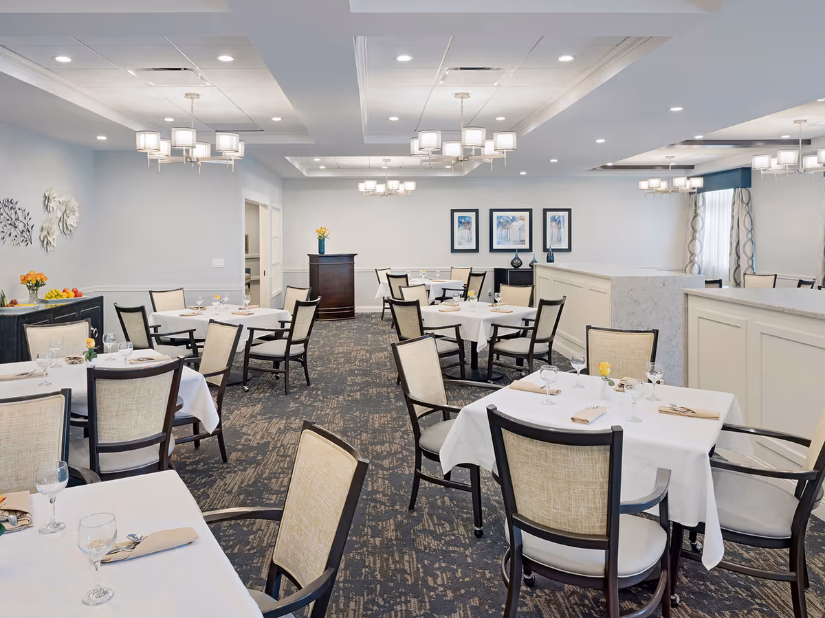 Bright, elegant dining room with multiple set tables and upholstered chairs under modern chandeliers.