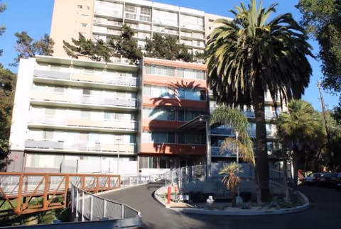Exterior view of a multi-story senior living building with palm trees and a ramp.