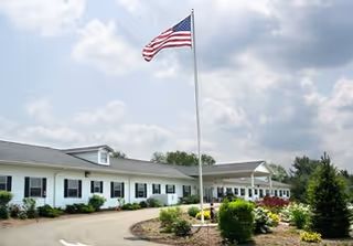 A single-story senior living facility with a tall American flag and manicured landscaping.