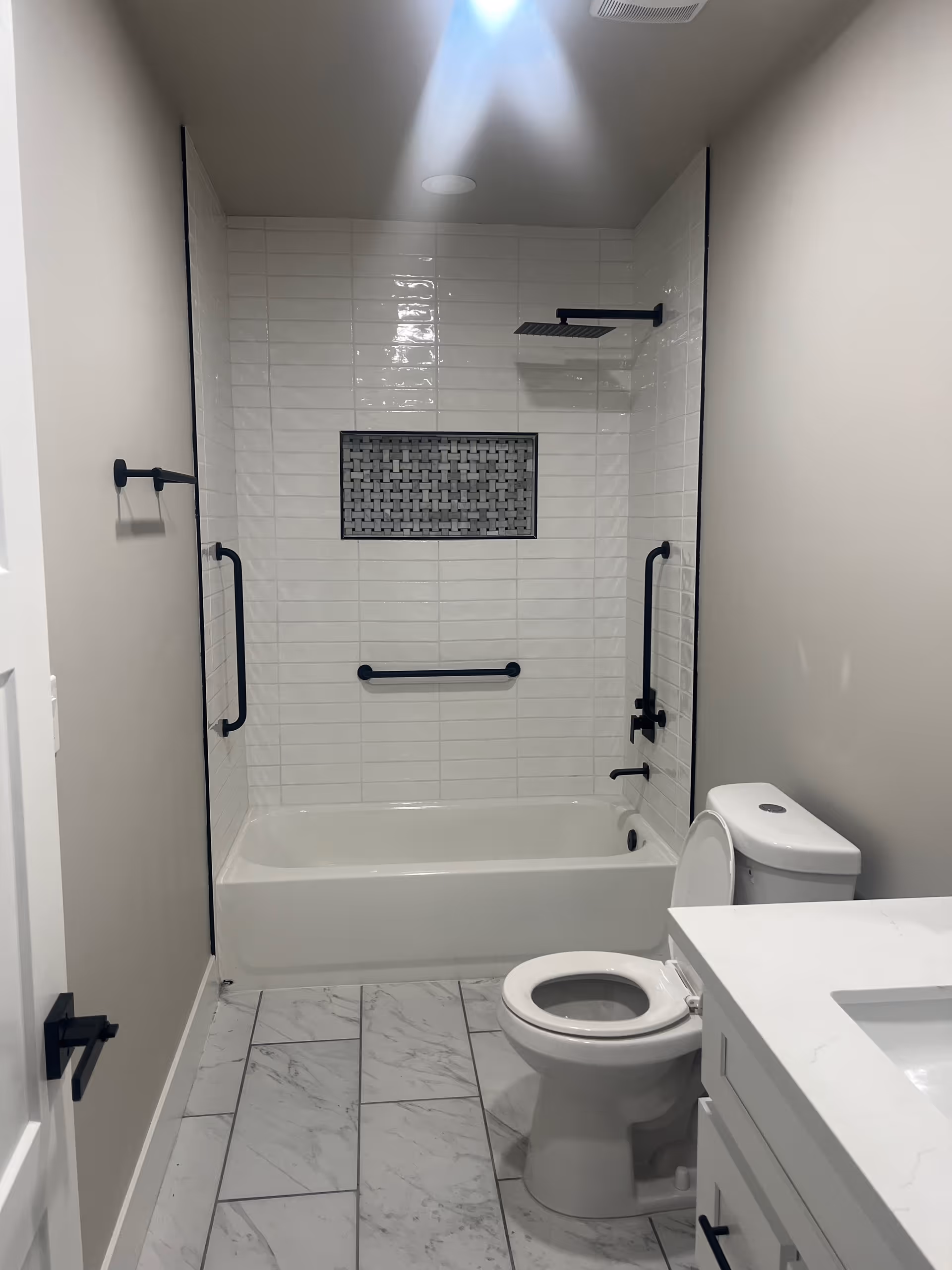 Modern bathroom with a white tub and tiled shower, black fixtures, a toilet, and a vanity.
