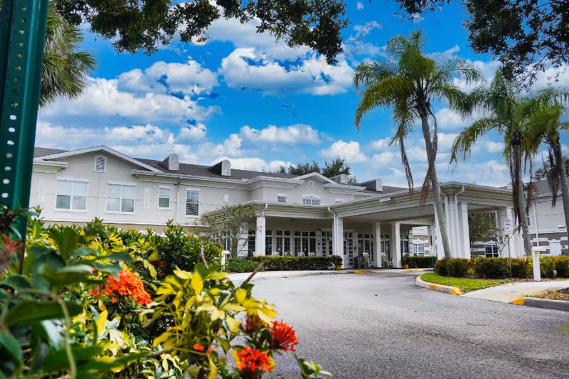 A senior living facility's daytime exterior with a covered entrance and palm trees.